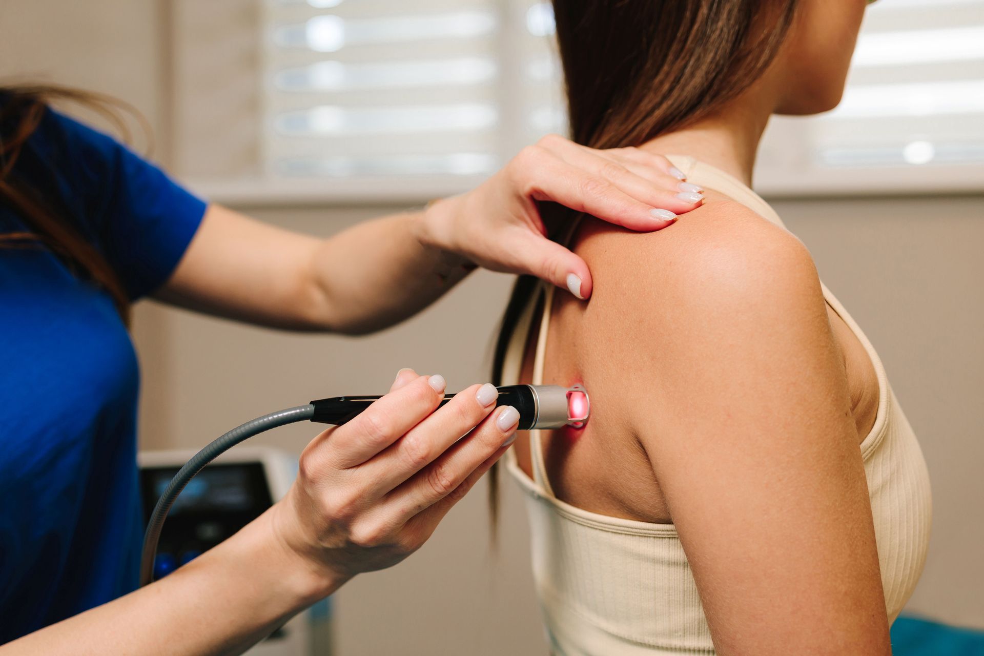 A practitioner applies a handheld red light therapy device to a patient's shoulder in a clinical setting.