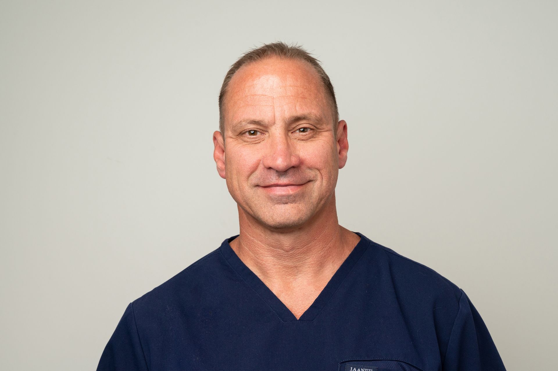 A man in a blue scrub top is smiling for the camera.