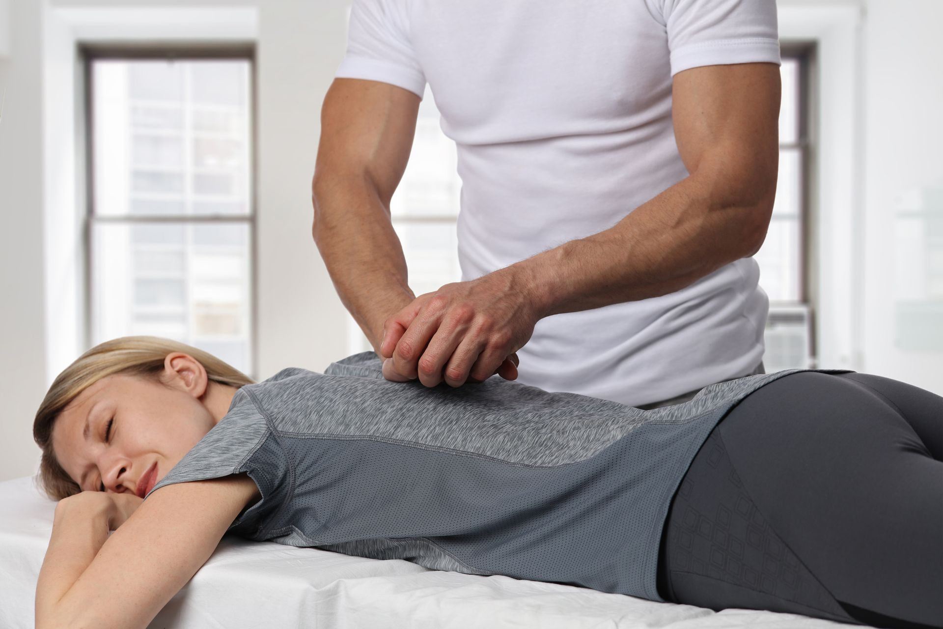 Chiropractor performing spinal adjustment on female patient lying on treatment table.