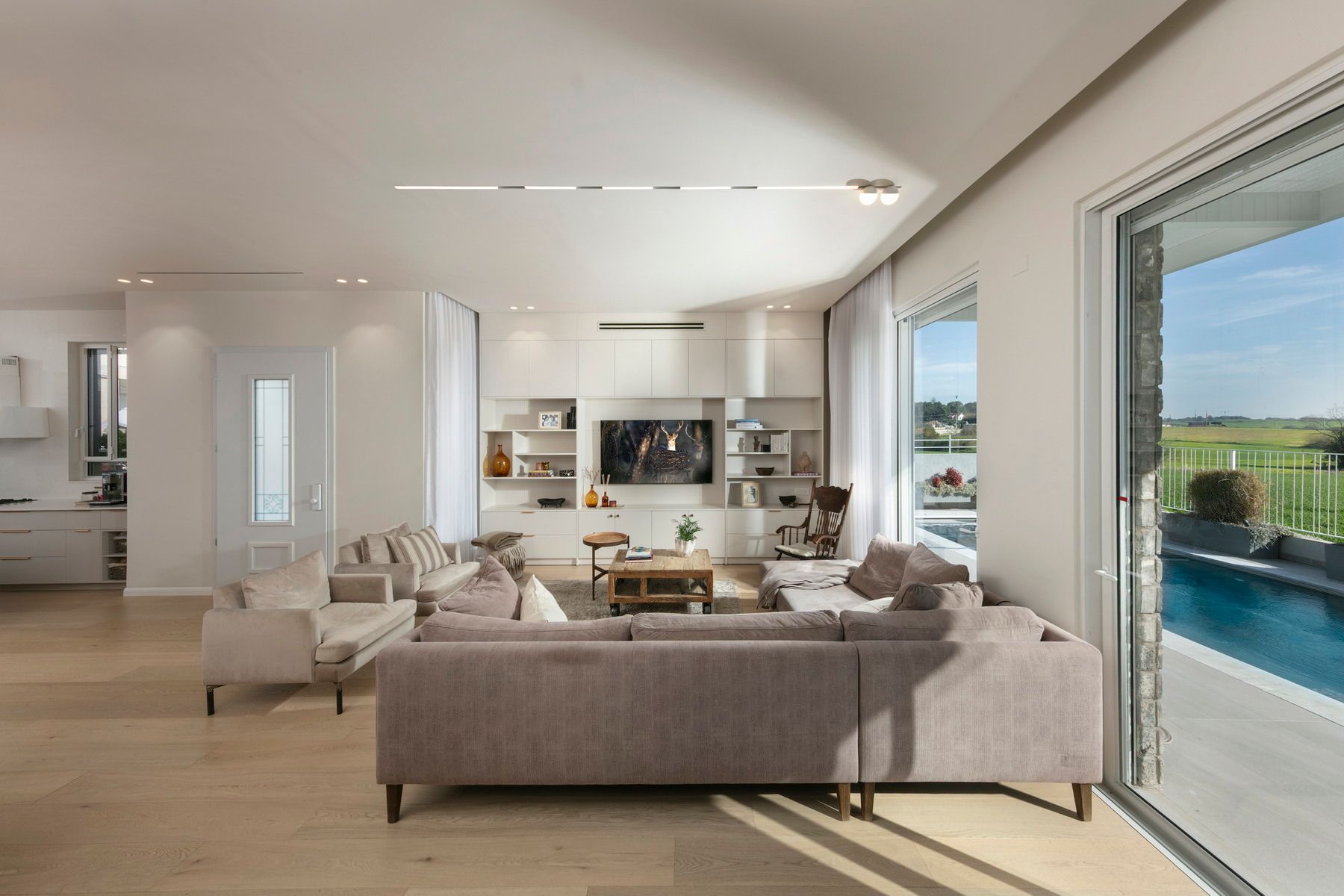 סלון מודרני ומואר עם ספה נפתחת, טלוויזיה ודלת הזזה מזכוכית לאזור בריכה.