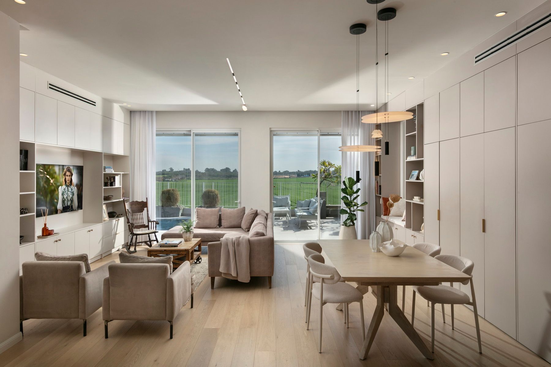 סלון מודרני עם רצפות עץ בהירות, ריהוט ניטרלי ונוף לשדה ירוק.