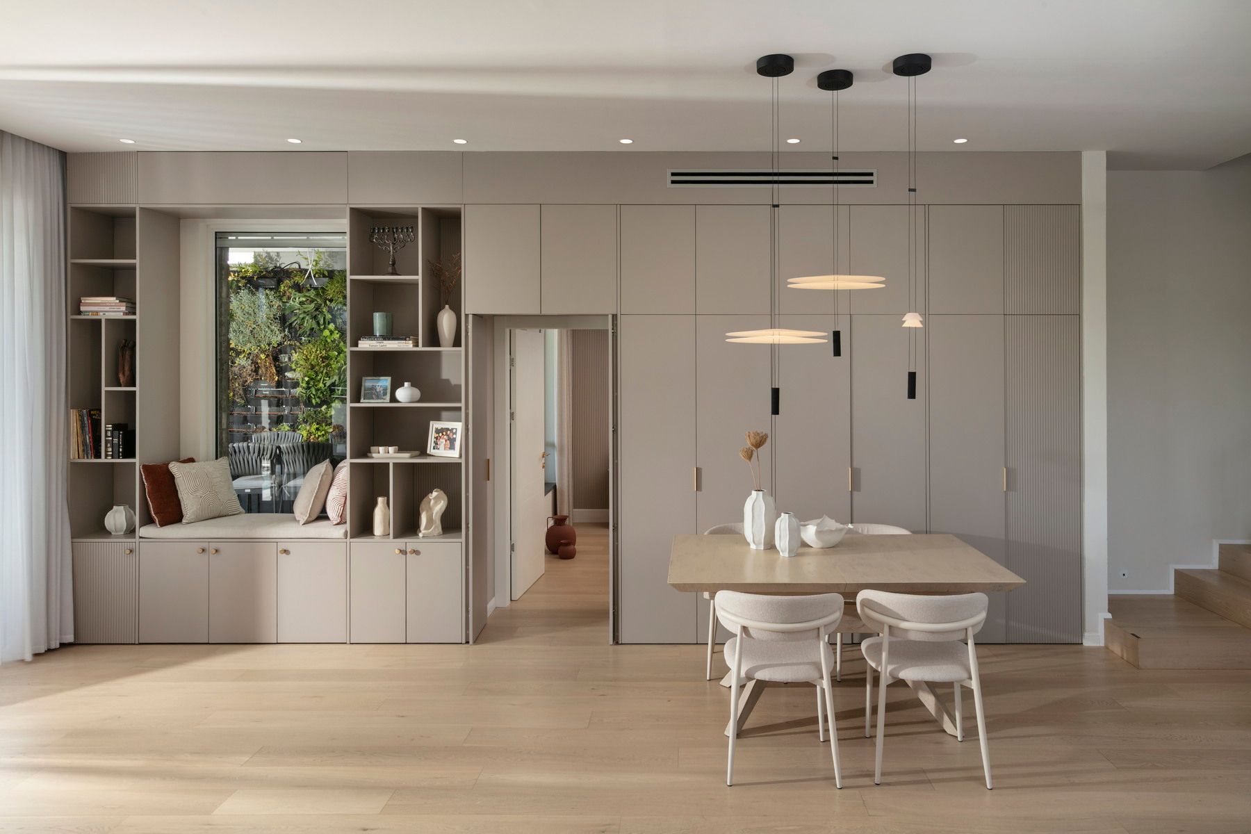 פינת אוכל מודרנית עם צבעים ניטרליים, מדפים מובנים, שולחן עם כיסאות ואור טבעי.