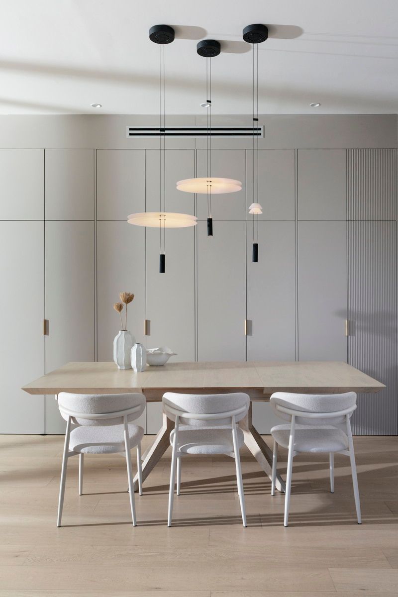 חדר אוכל עם מנורות תליון מודרניות, שולחן עץ וכיסאות לבנים. קירות בצבע בז' בהיר.
