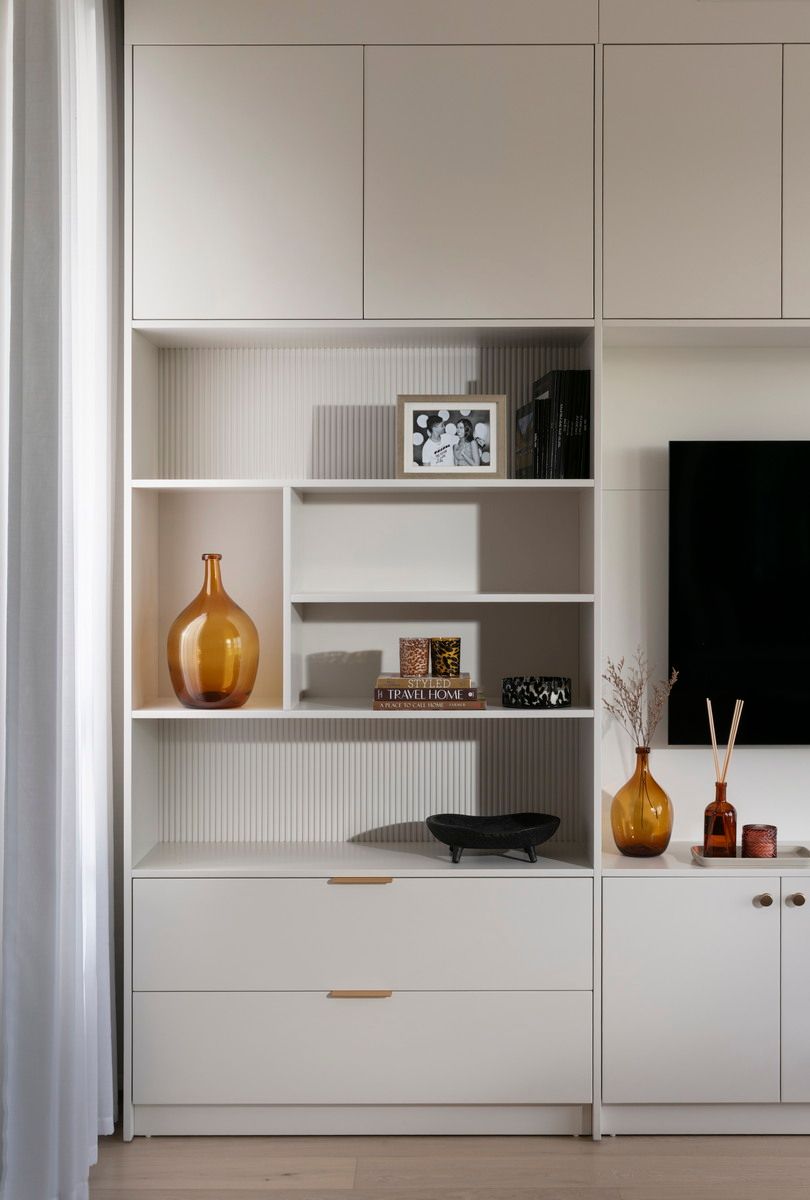 יחידת מדפים לבנה מובנית עם פריטי נוי: אגרטלים, תמונה ממוסגרת וקערה שחורה.