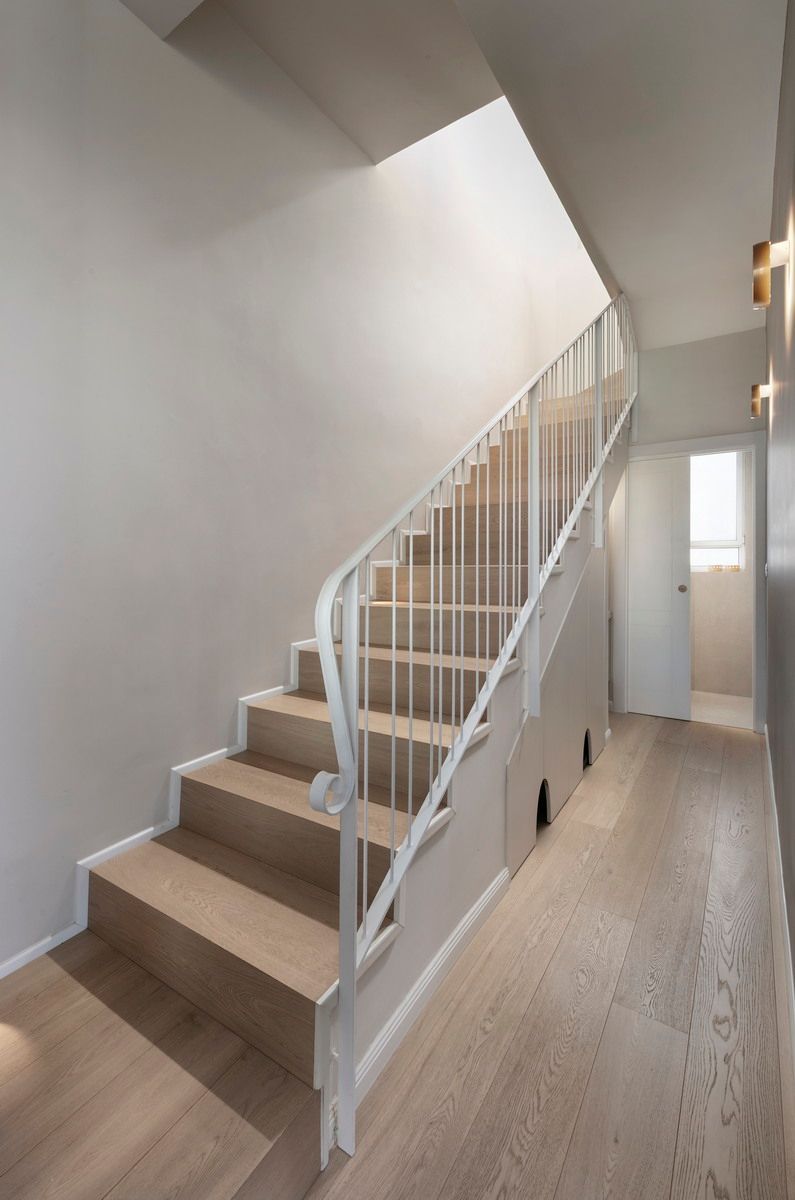 גרם מדרגות עם מעקה לבן ומדרגות עץ, המוביל לקומה עליונה. מסדרון עם ריצוף עץ בהיר.