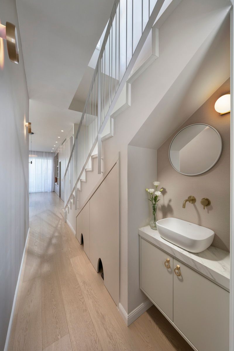 מסדרון צר עם מדרגות, חדר שירותים מתחת למדרגות וריצוף עץ בהיר.