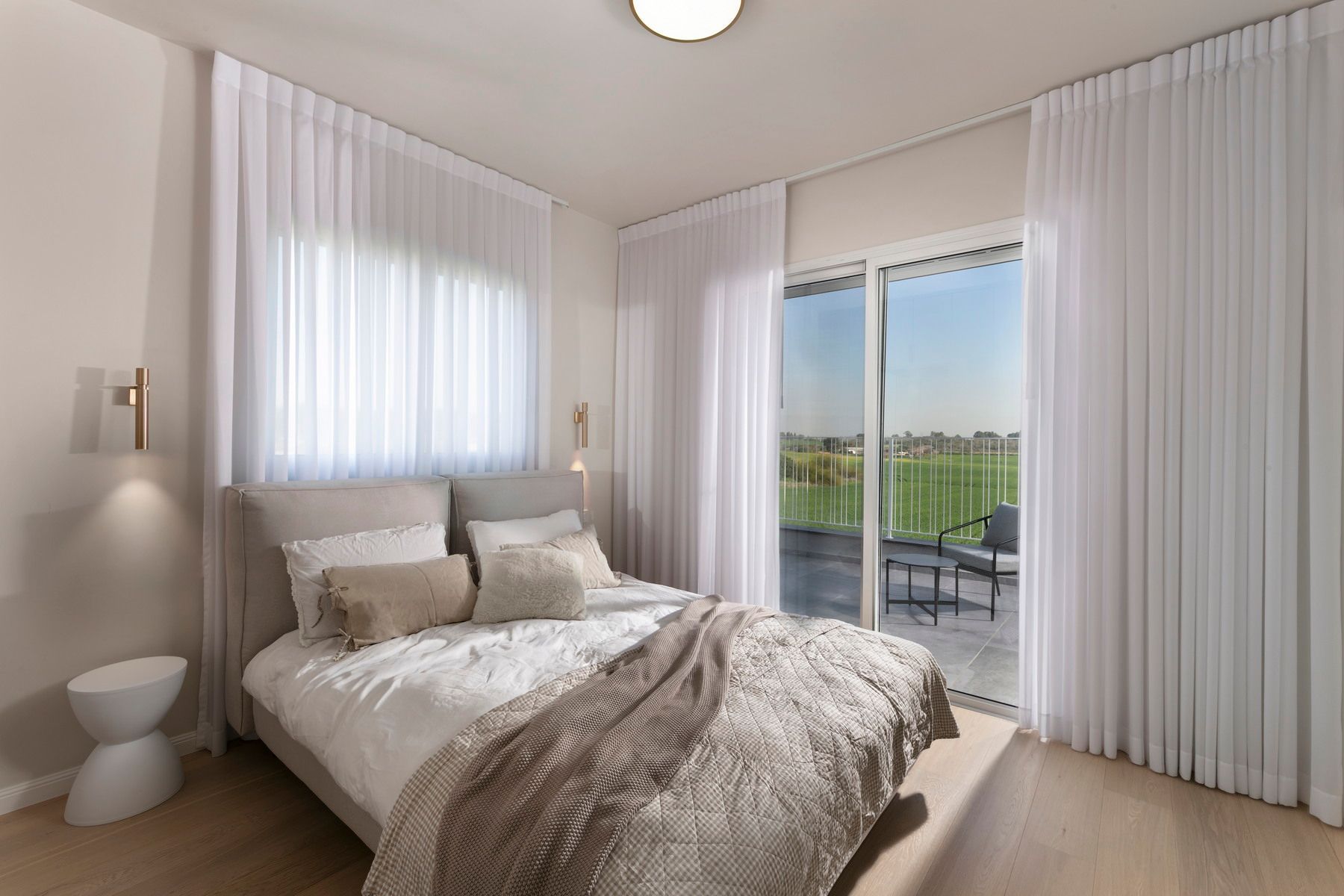 חדר שינה עם מיטה, וילונות לבנים שקופים ונוף לפטיו עם כיסא.