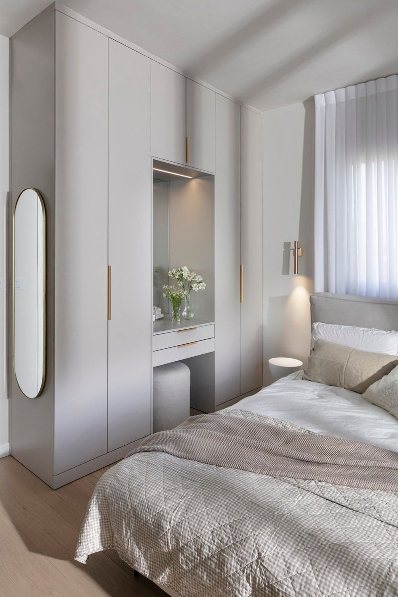 חדר שינה עם ארון בגדים אפור בהיר וכיור. מיטה עם מצעים בצבע בז' ניצבת מול הארון.