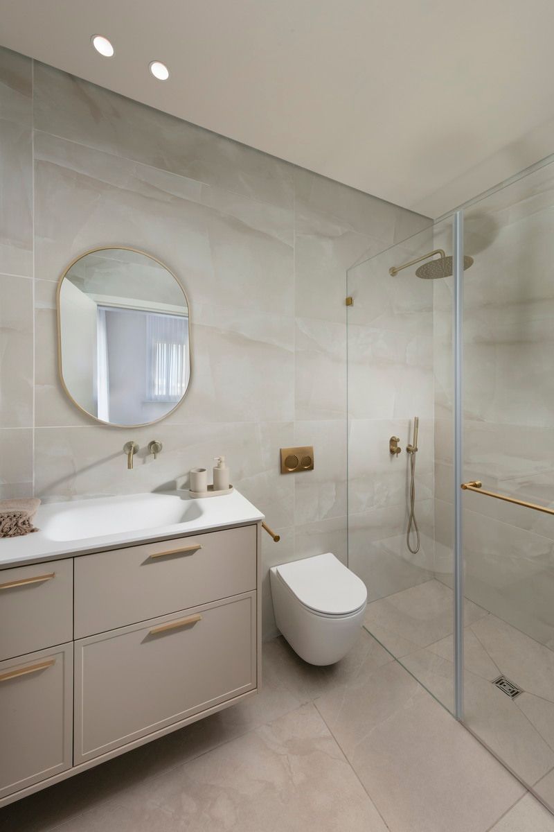 חדר רחצה מודרני עם מקלחון זכוכית, אסלה, כיור ומראה עגולה.