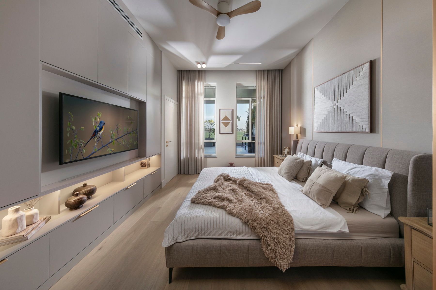 חדר שינה עם מיטה גדולה, טלוויזיה על הקיר, צבעים ניטרליים ונוף החוצה.