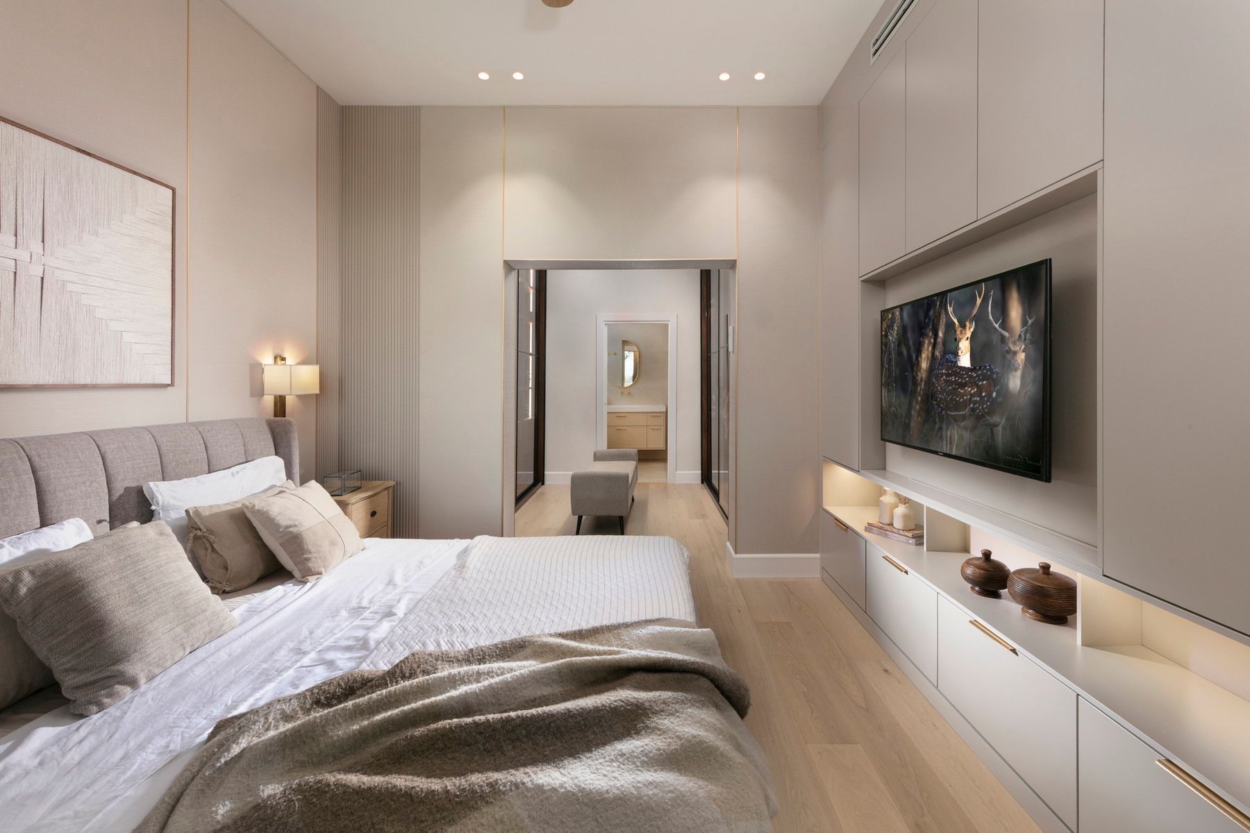 חדר שינה נעים עם מיטה, טלוויזיה ודלת הזזה לחדר רחצה; גוונים ניטרליים, עיצוב מודרני.