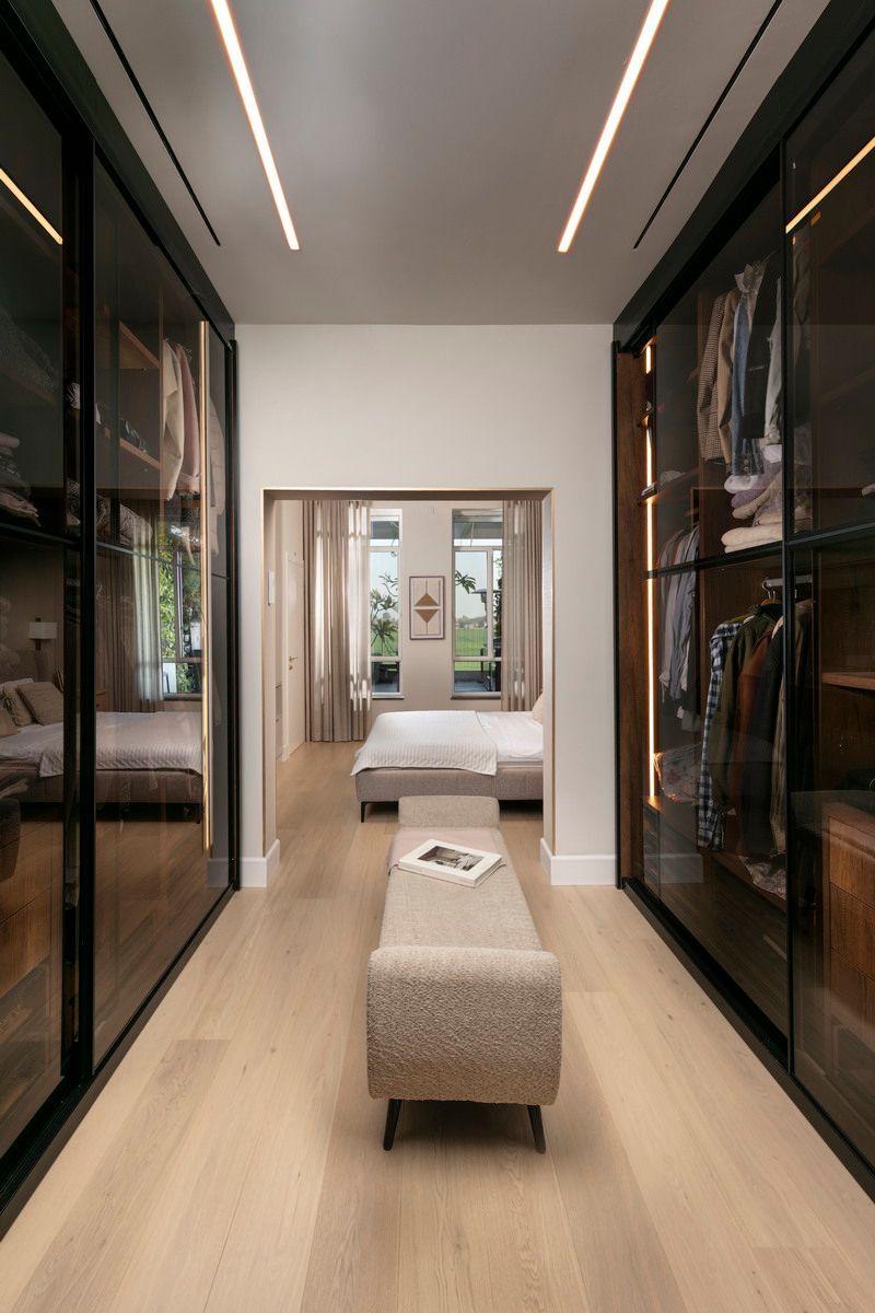 חדר ארונות עם דלתות זכוכית כהה וריצוף עץ בהיר, ספסל, המוביל לחדר שינה.