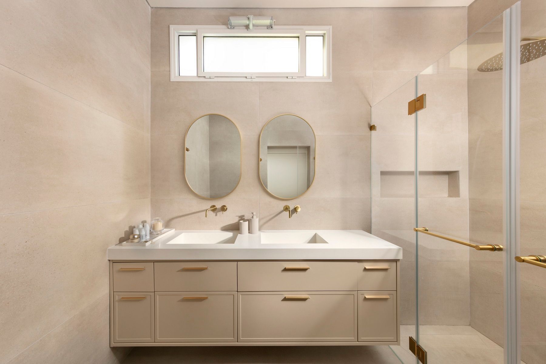 חדר אמבטיה בצבע בז' עם כיור כפול, מראות אובליות ומקלחון מזכוכית.