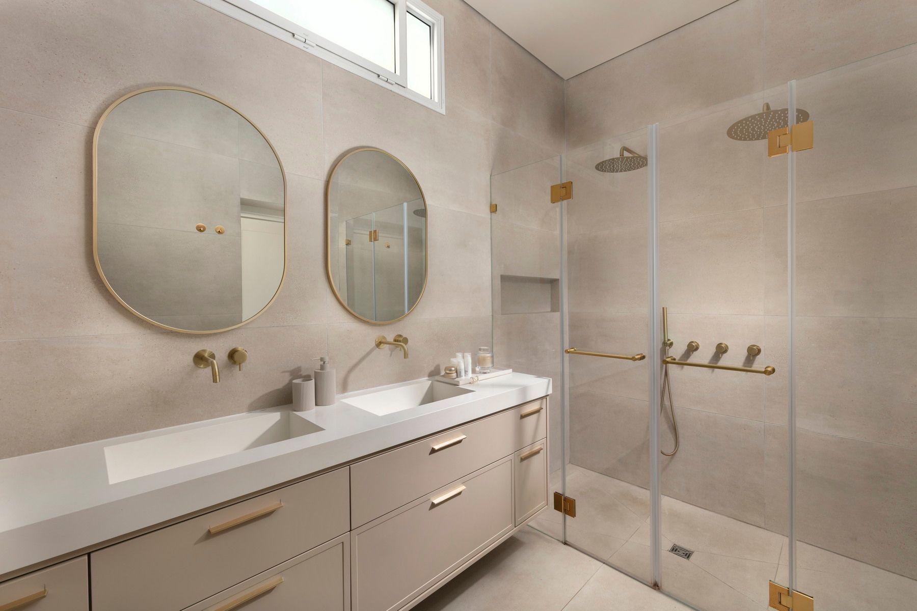 חדר אמבטיה מודרני בצבע בז' עם כיורים כפולים, מראות אובליות ומקלחון מזכוכית.