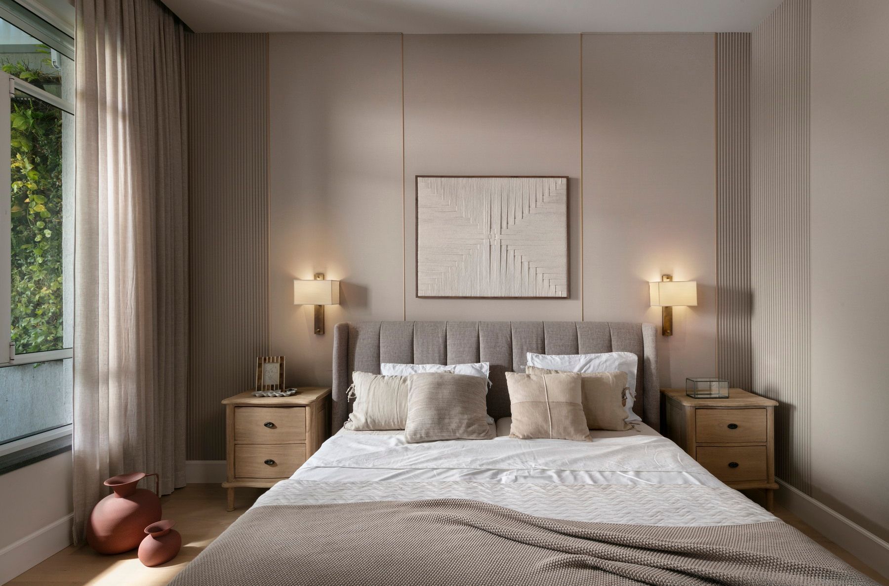 חדר שינה עם גוונים ניטרליים, מיטה, יצירות אמנות, שידות לילה, חלון עם וילונות ותאורה חמימה.