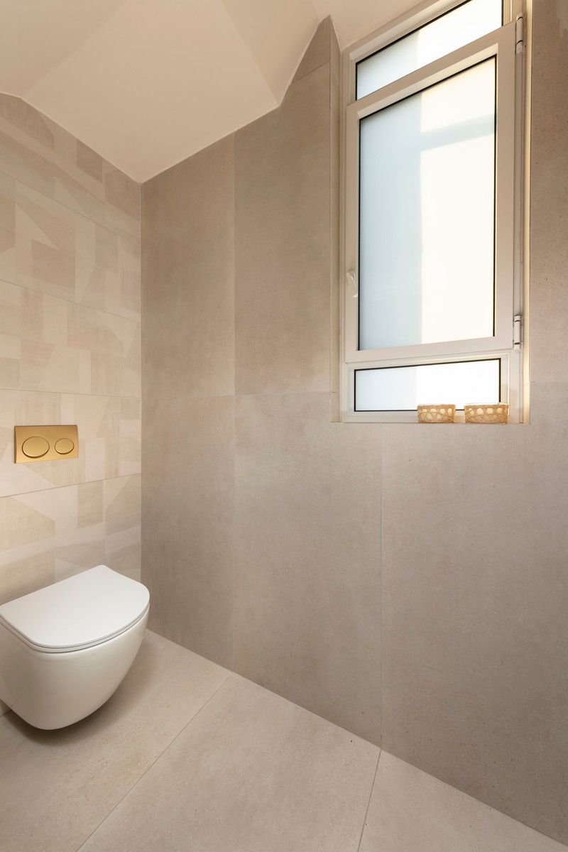 חדר רחצה מודרני עם אריחים בצבע בז', אסלה לבנה וחלון עם אור חזק.