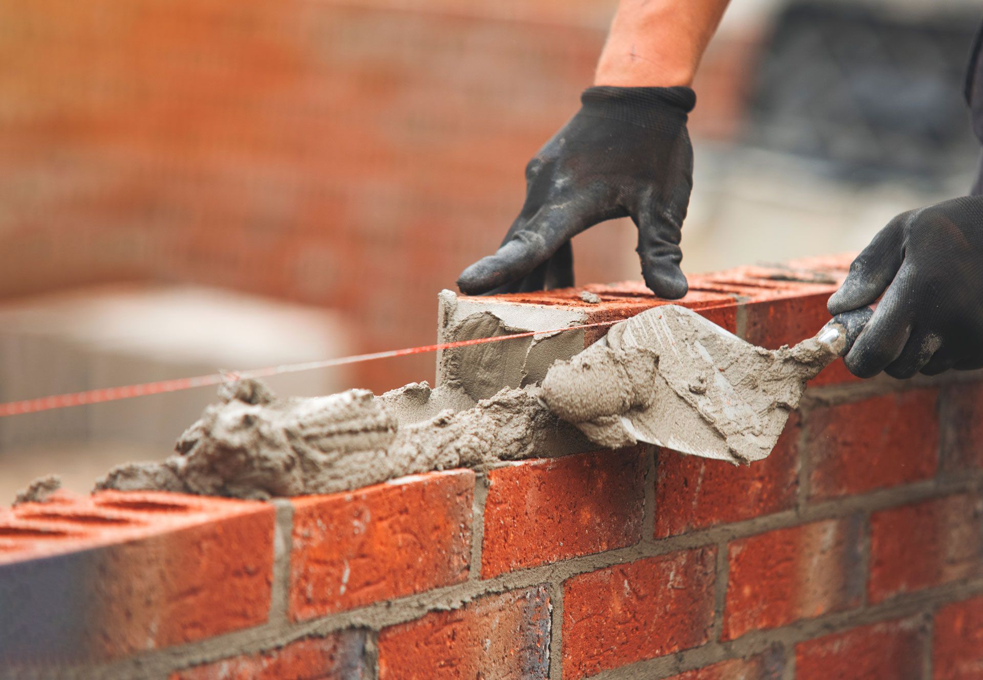 Gloved hands laying wet mortar on a red brick wall during construction