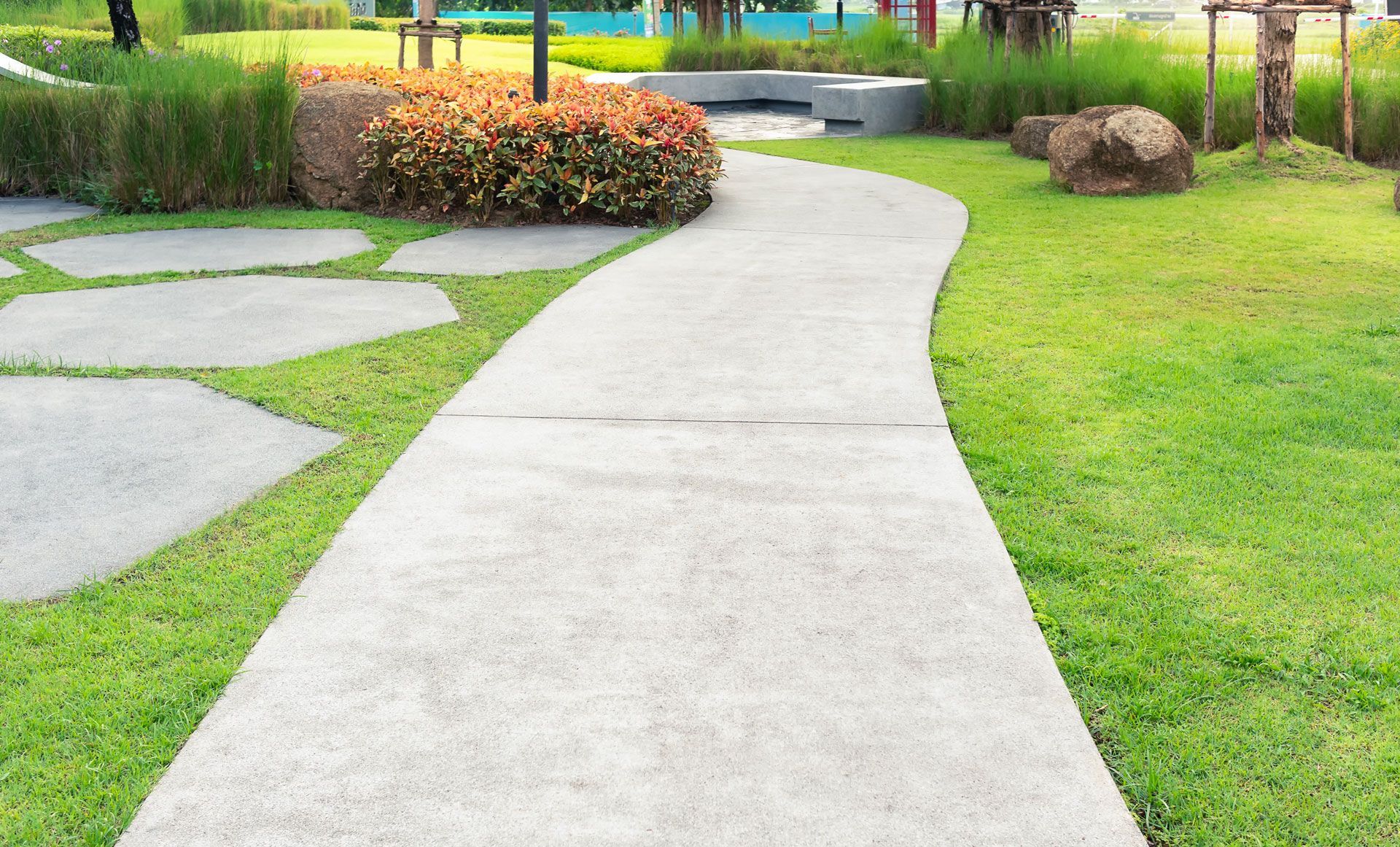 Curving concrete garden path beside green grass and landscaped shrubs in a park