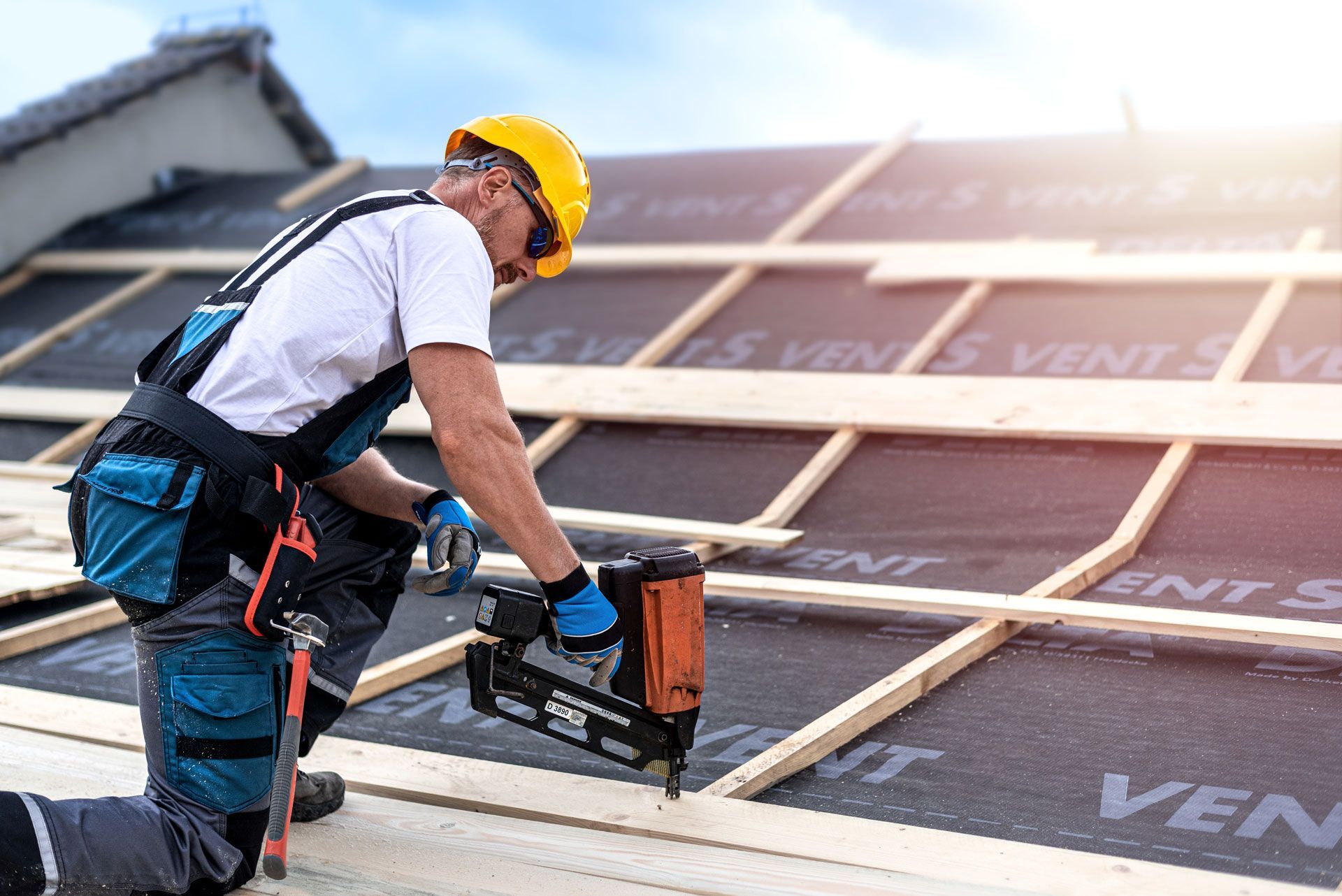 Worker in yellow hard hat installing solar panels on a rooftop with a nail gun.