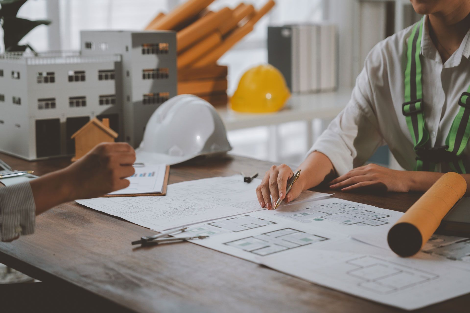 People reviewing architectural plans at a construction site table with hard hats and blueprints