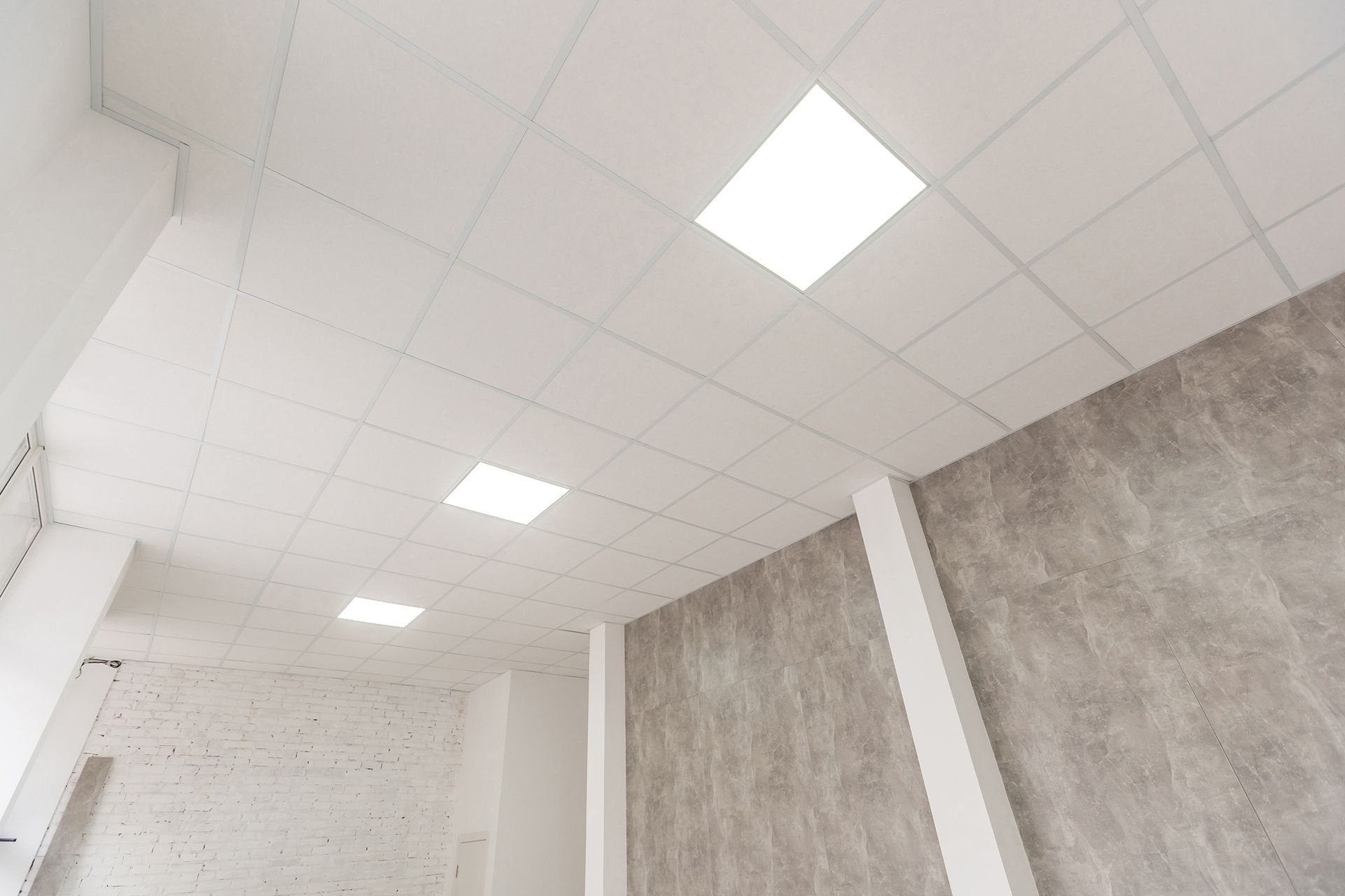 White drop ceiling with square lights above textured gray walls in an empty interior room