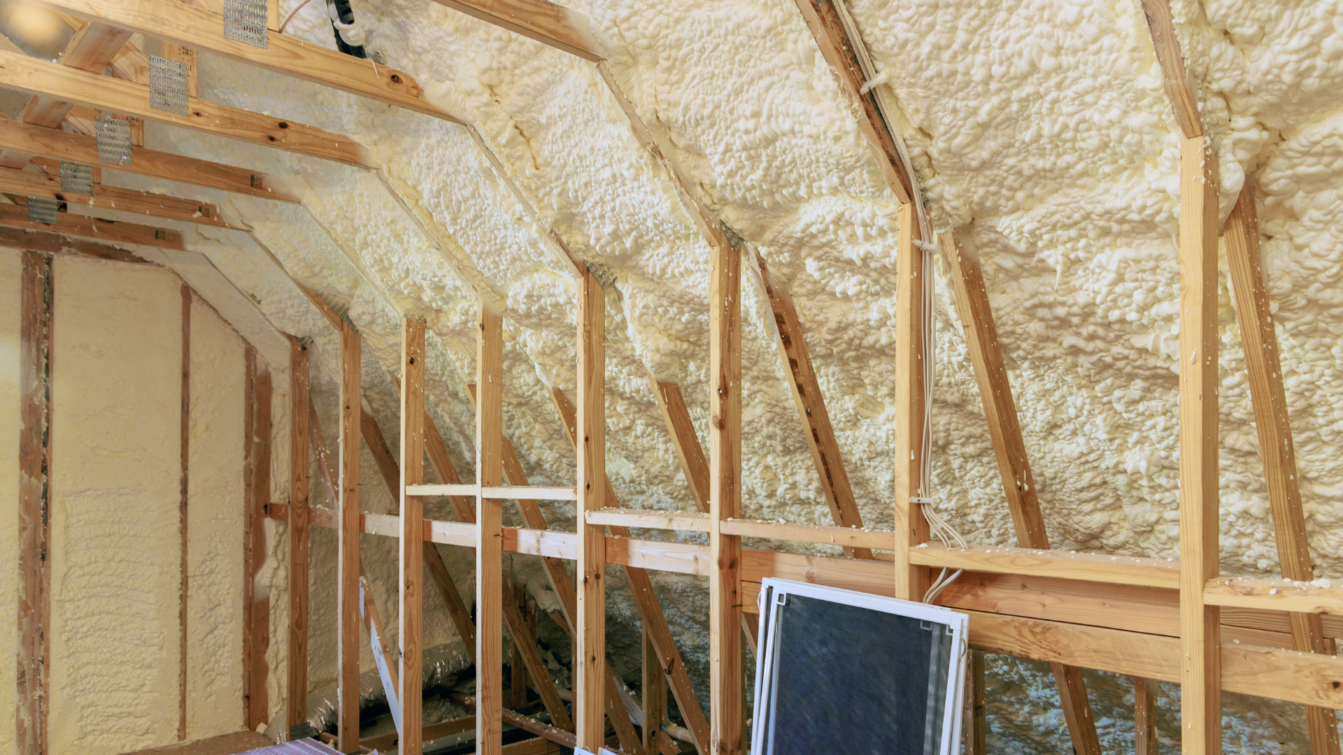 Attic interior with spray foam insulation between wooden rafters.