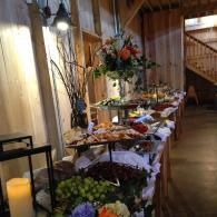 Decorated buffet table in a dim hallway with flowers, trays of food, and a staircase in the background