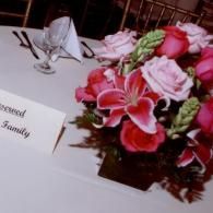 Pink floral centerpiece beside a wedding place card on a white tablecloth