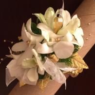 White floral corsage on a tan ribbon-wrapped wrist, with cream flowers and gold accents