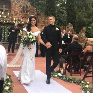 Bride and groom walking down a flower-lined aisle at an outdoor wedding ceremony