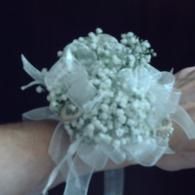 White floral wrist corsage with sheer ribbon on a wrist against a dark background