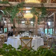 Rustic dining room with round tables, white tablecloths, wooden chairs, and greenery decor