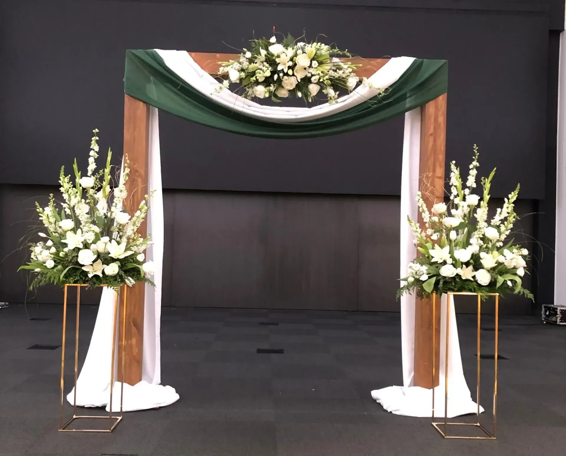 Decorated wedding arch with white flowers and green drapes on a dark stage