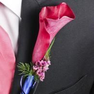 Pink calla lily boutonniere with purple flowers and greenery on a black suit lapel