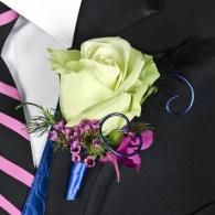 Light green rose boutonniere with purple flowers pinned to a black suit jacket and striped tie