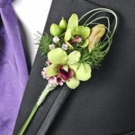 Green and white boutonniere with purple accents pinned to a dark suit lapel and lavender tie