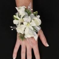 White floral corsage on a person’s wrist and hand against a black background