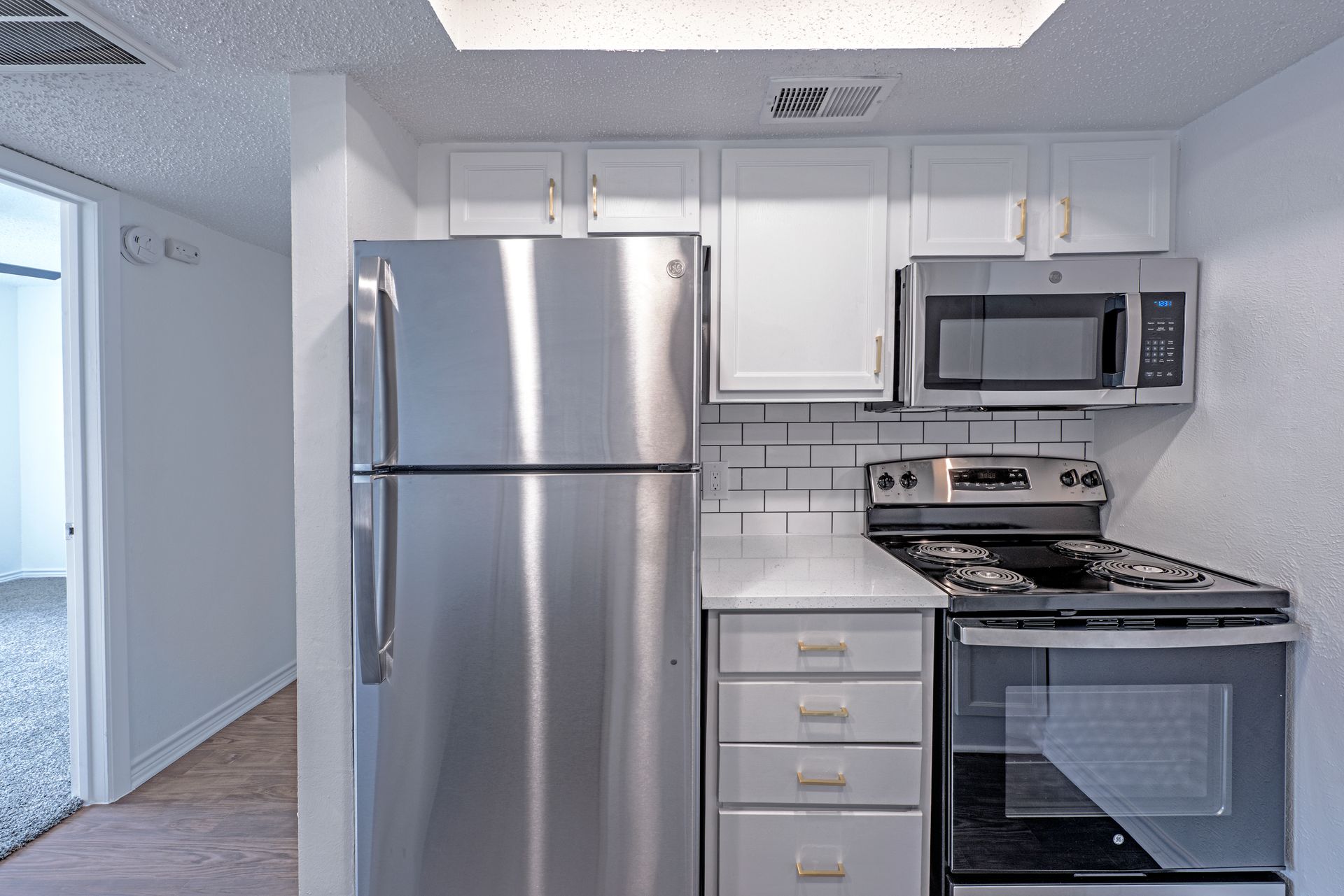 Small, white kitchen with stainless steel appliances.