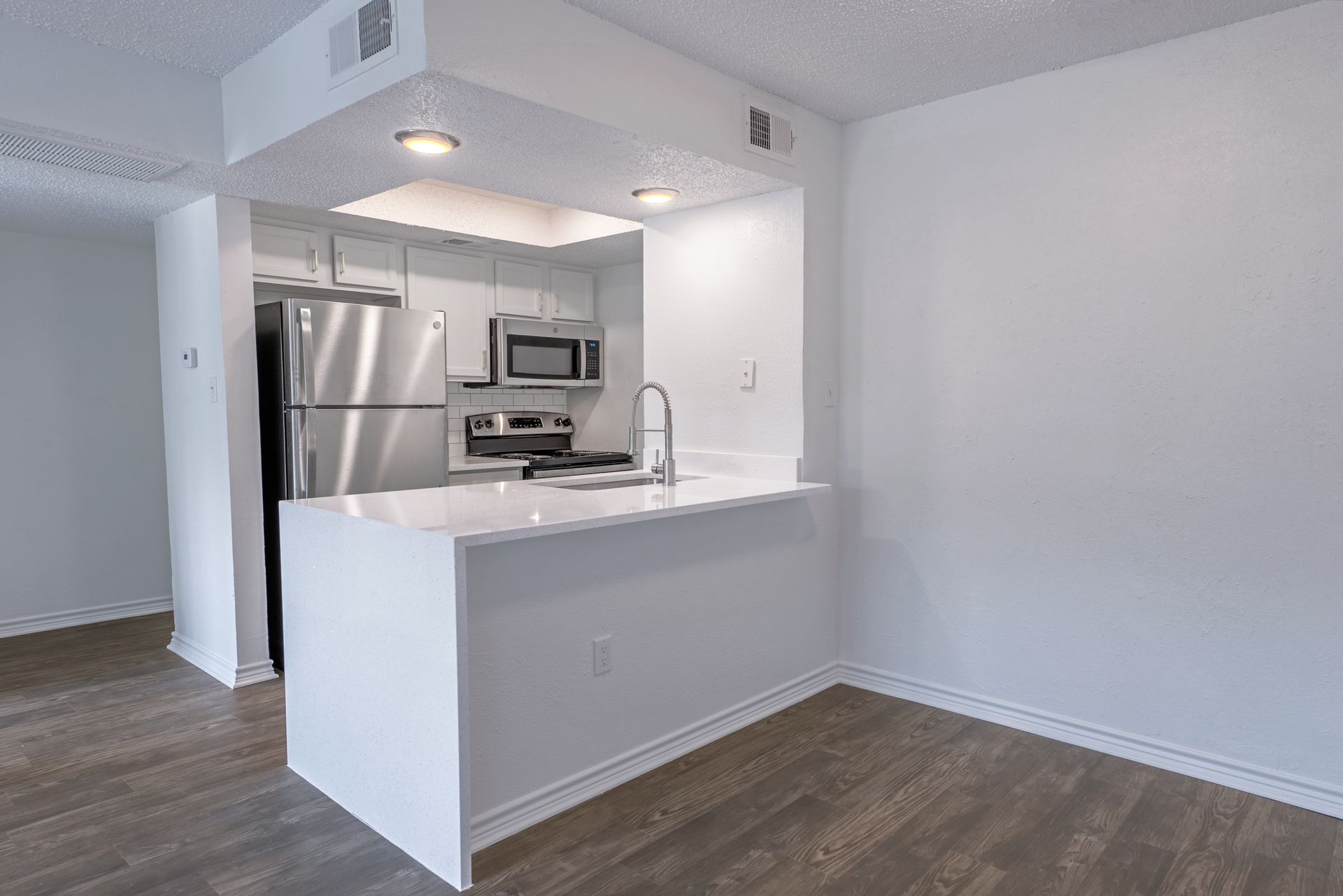 Modern kitchen with white island, stainless steel appliances, and wooden floors.