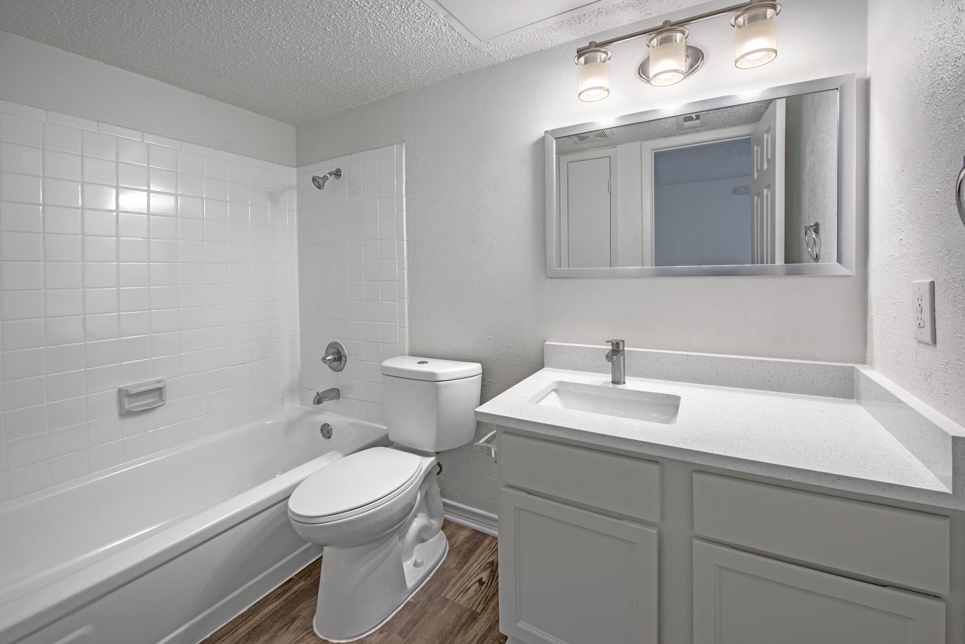 White bathroom with a tub, toilet, vanity, and mirror.