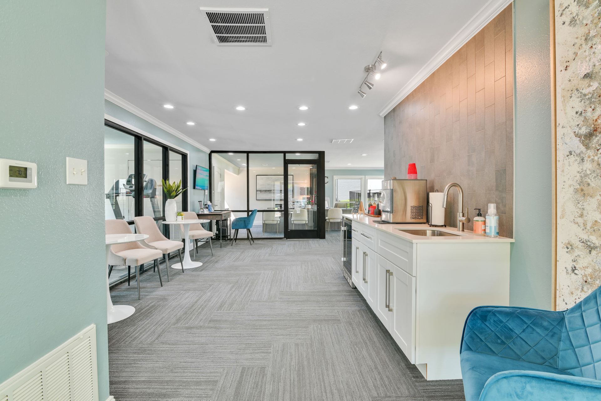 Interior of a modern office with desks, a kitchen, and a blue armchair.