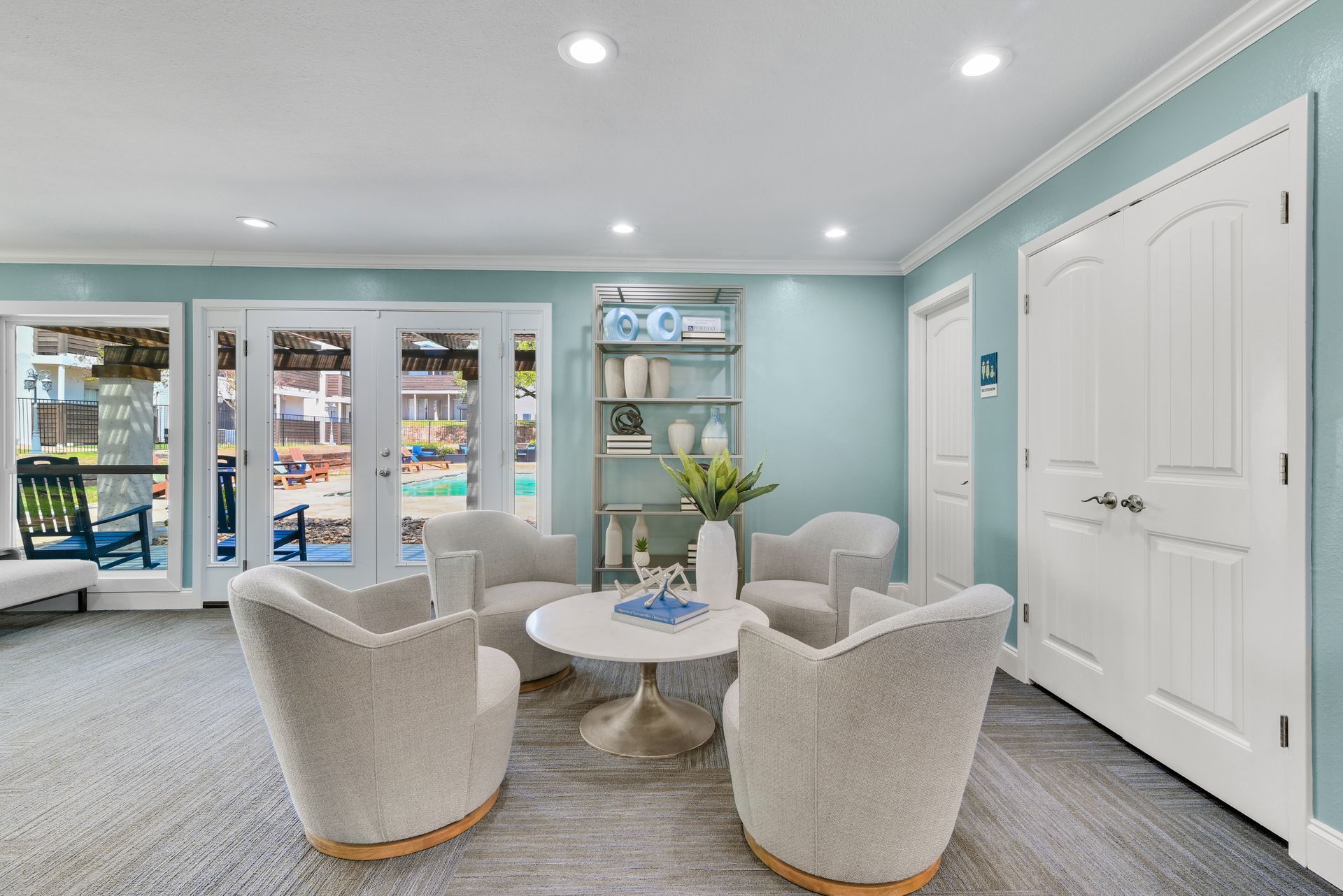 Living room with four white armchairs around a white table, blue walls, and double doors to a patio.