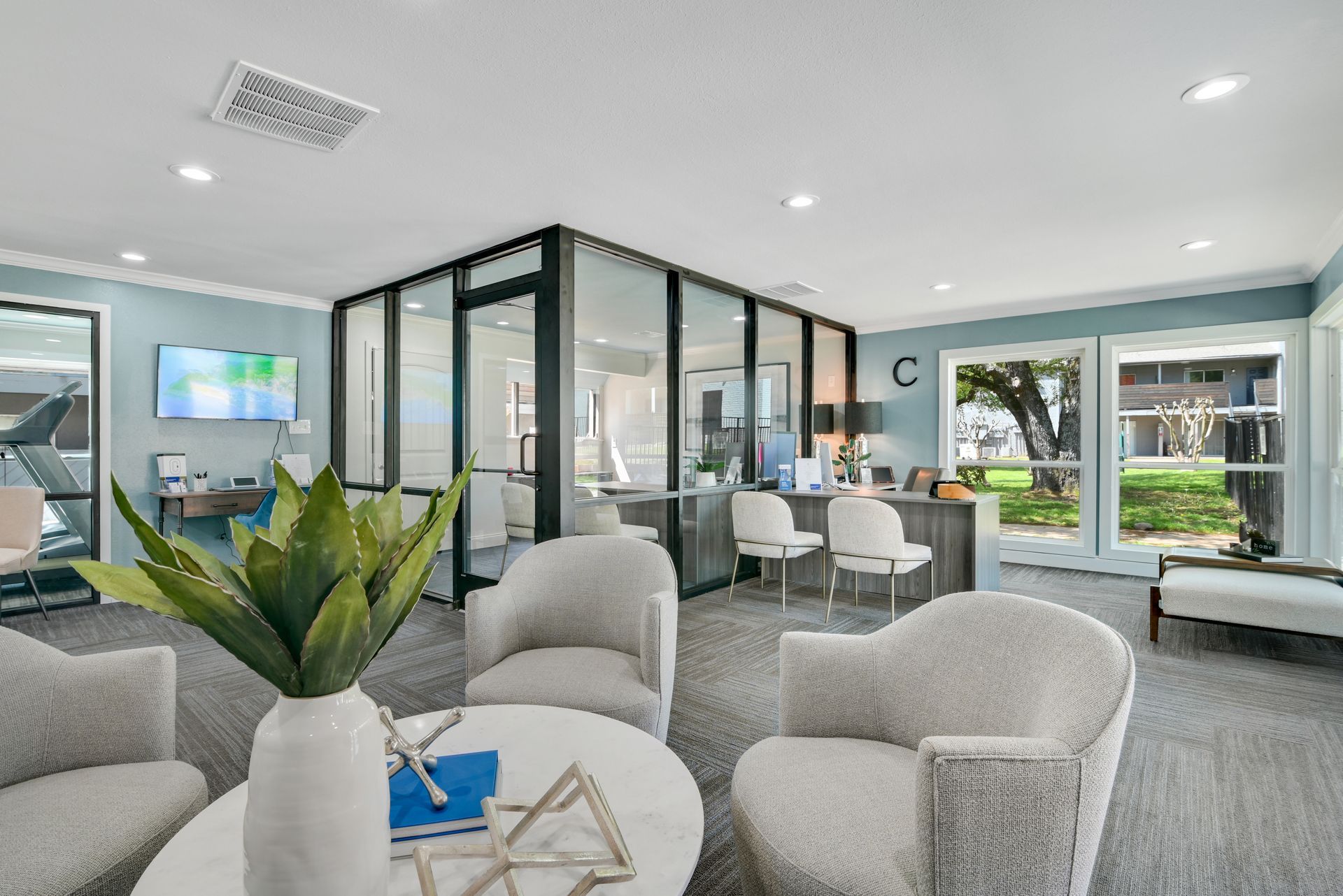 Cozy waiting room with neutral furniture, modern glass office, and outdoor view.