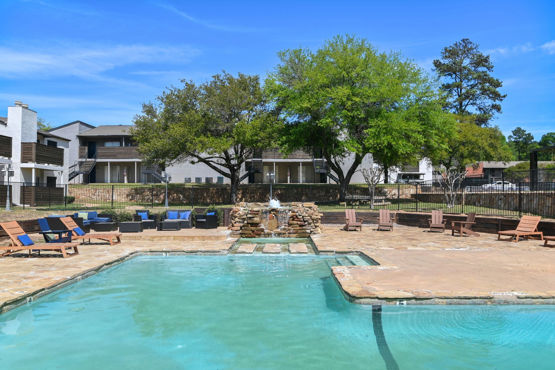 Swimming pool with lounge chairs, stone waterfall, and apartment buildings.
