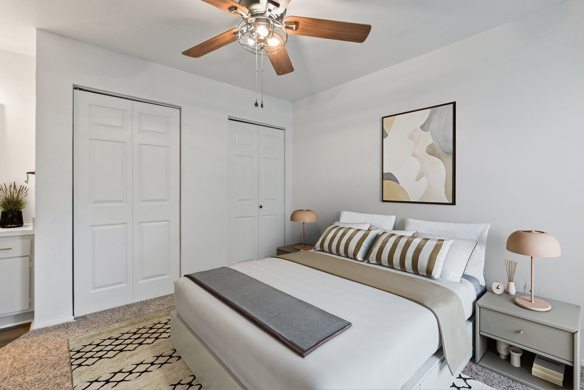 Bedroom with a bed, artwork, two closets, and a ceiling fan; neutral color scheme.