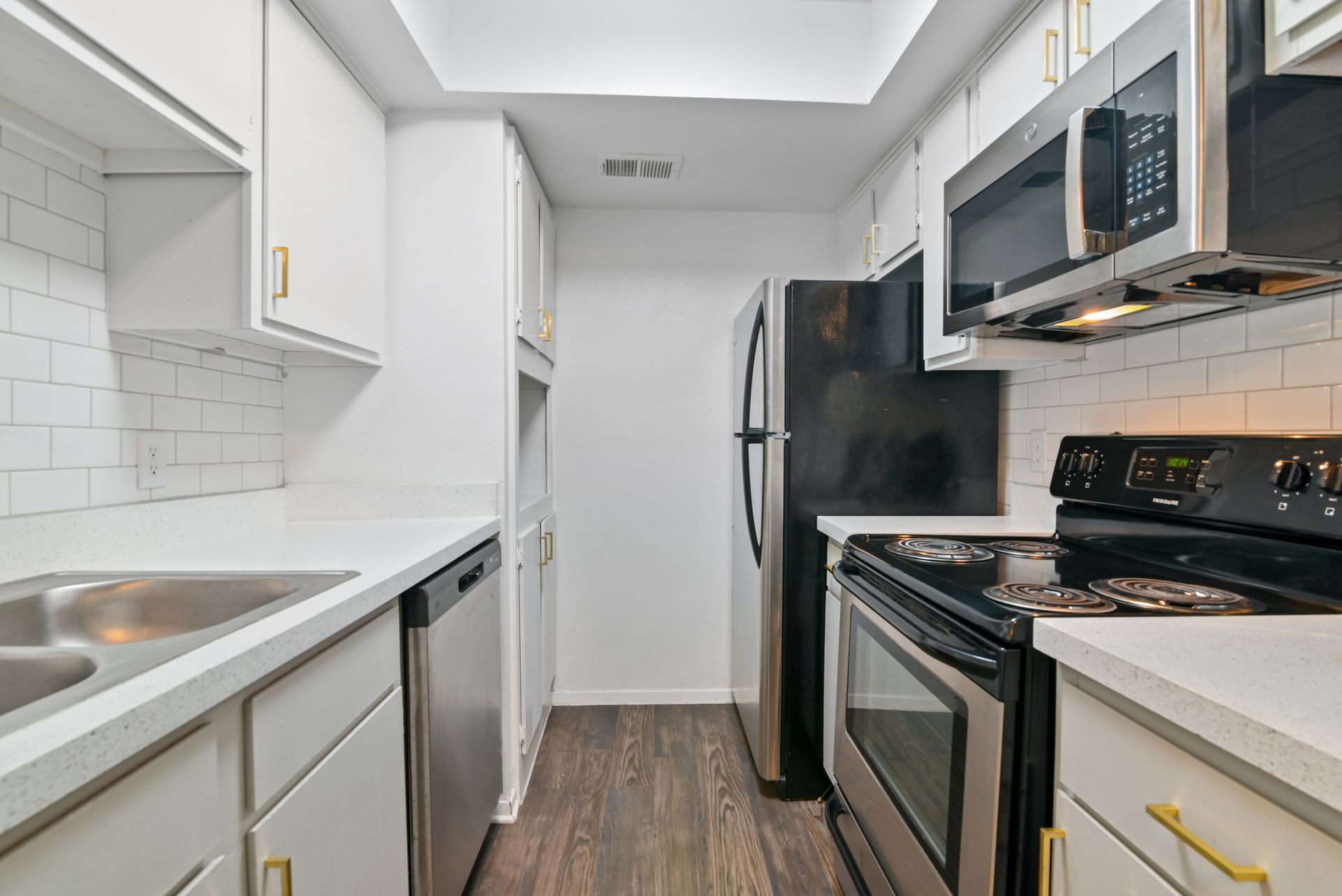 Narrow white kitchen with stainless steel appliances and dark flooring.