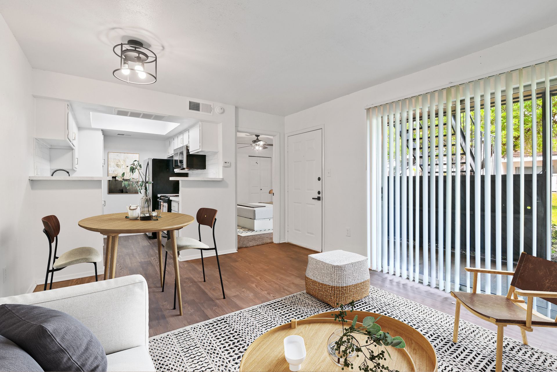 Cozy apartment living room with round table, white couch, sliding glass door, and wooden floor.