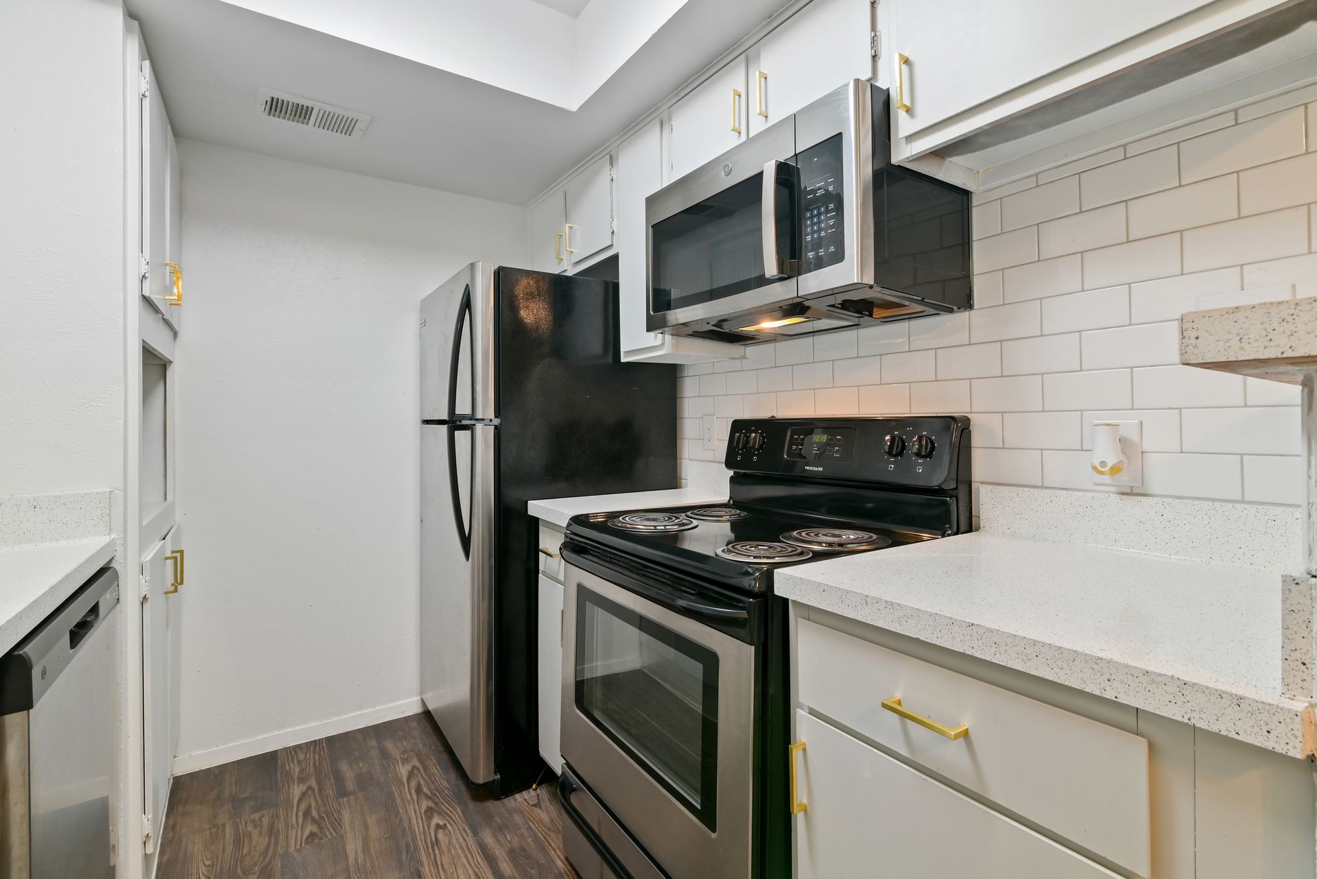 Small kitchen with white cabinets, stainless steel appliances, and dark wood floor.