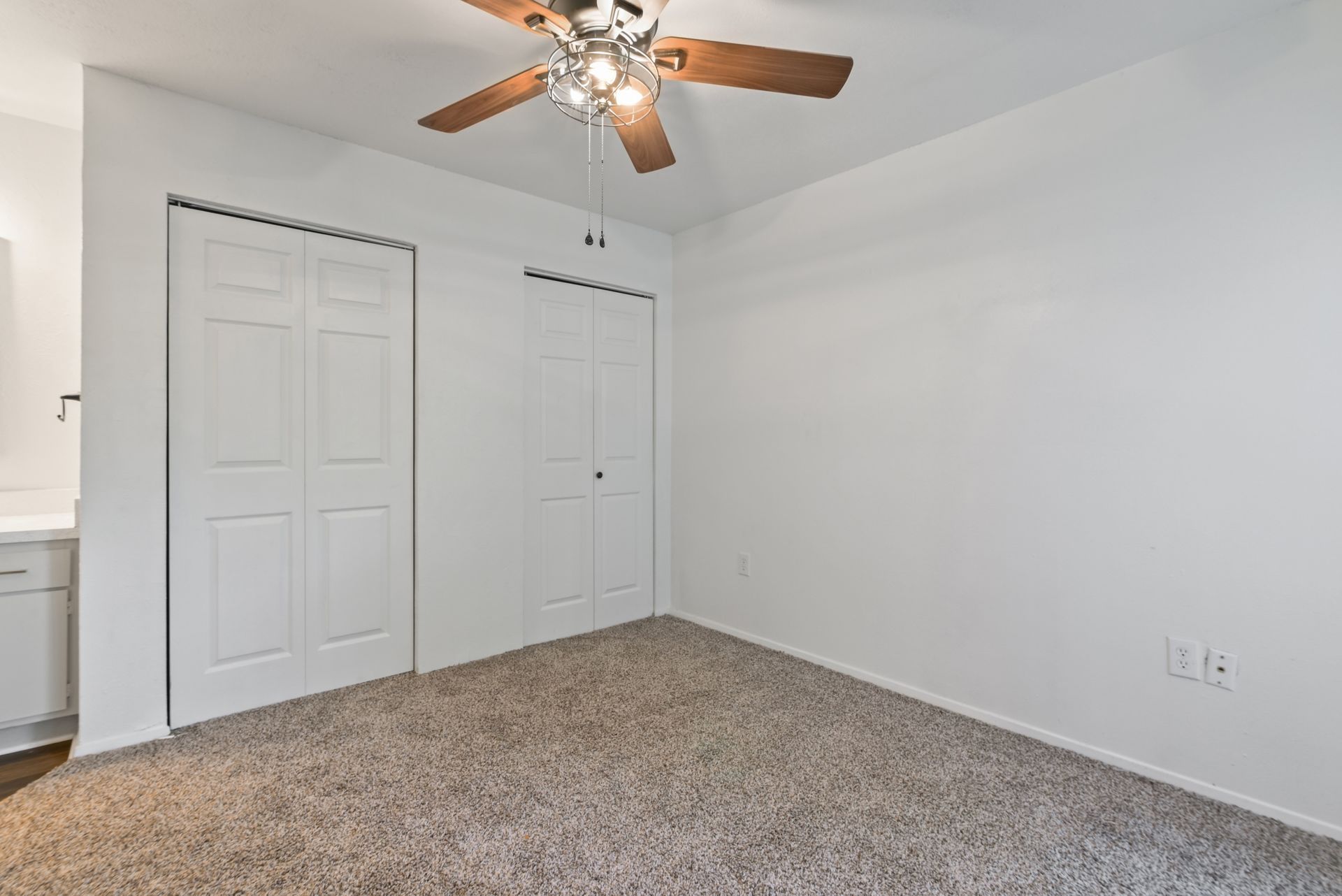 Empty bedroom with white walls, carpet, two doors, and a ceiling fan.