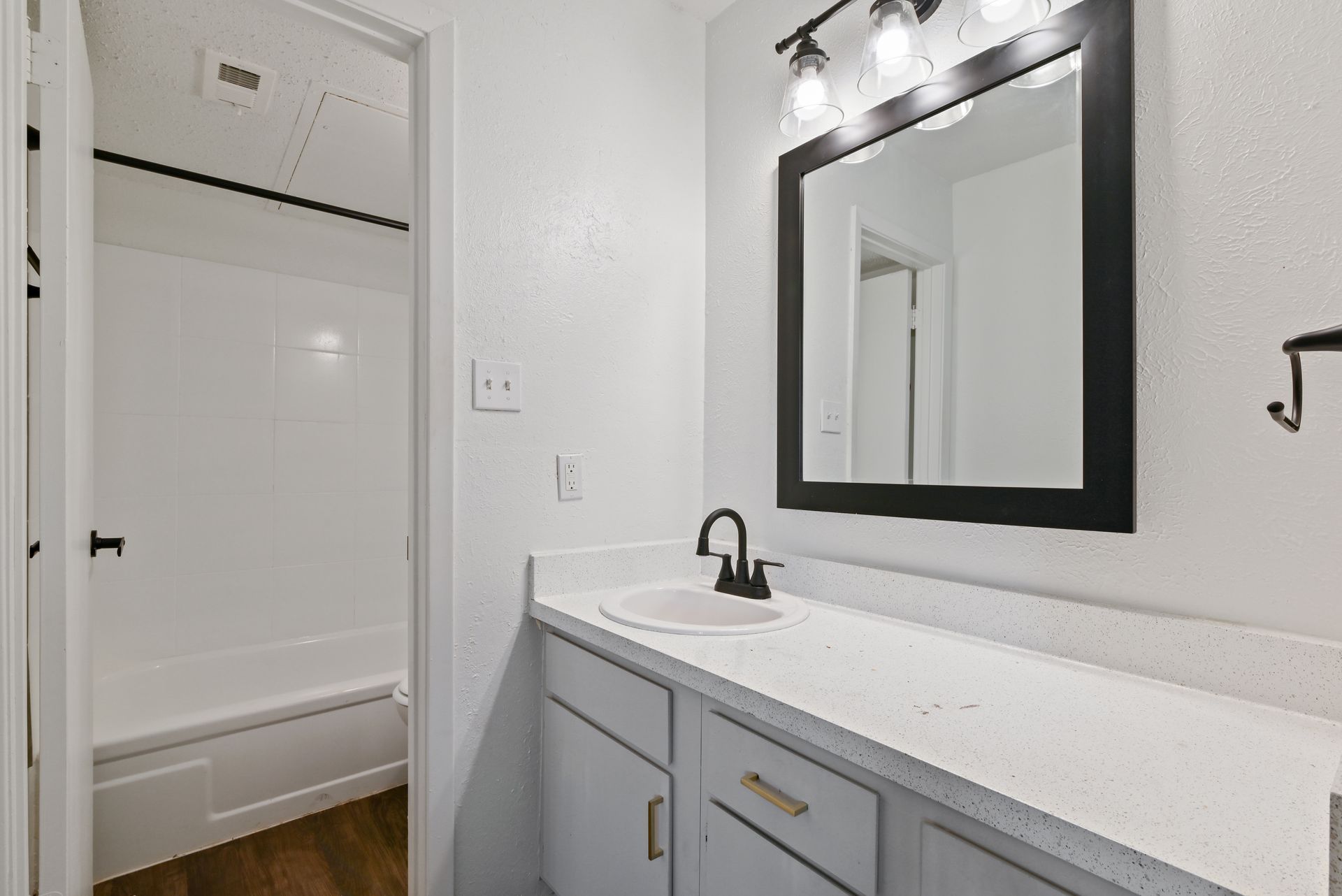 White bathroom with black accents: vanity, mirror, faucet, and door handle. Includes a shower/tub.